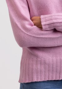 Jasnoróżowy sweter z dzianiny z prążkowanym dołem i mankietami. Miękka tekstura, luźny krój i podwinięte rękawy, eksponujące detale ściegów przędzy.