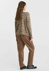 Maglione a stampa leopardata in beige e marrone, vestibilità oversized; abbinato a pantaloni marroni con texture e scarpe nere. Vista posteriore mostrata.