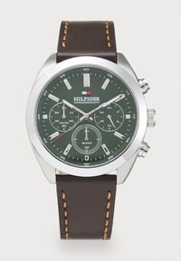 Montre chronographe avec un cadran vert, un boîtier en acier inoxydable argenté et un bracelet en cuir brun avec des coutures contrastantes et des sous-cadrans.