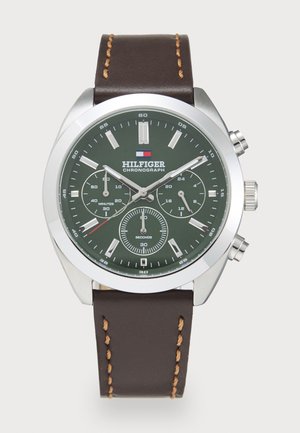 Montre chronographe avec un cadran vert, un boîtier en acier inoxydable argenté et un bracelet en cuir brun avec des coutures contrastantes et des sous-cadrans.