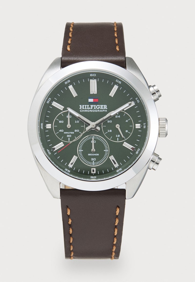 Montre chronographe avec un cadran vert, un boîtier en acier inoxydable argenté et un bracelet en cuir brun avec des coutures contrastantes et des sous-cadrans.