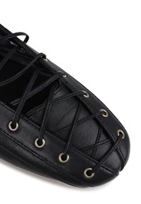 Chaussure en cuir noir avec un laçage croisé et des œillets en argent. La texture est lisse, avec un bout rond et une semelle durable.