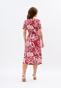 Rotes Blumenkleid mit kurzen Ärmeln und tailliertem Gürtel. Hergestellt aus leichtem Stoff mit einer glatten Textur, der weiße botanische Muster zeigt.