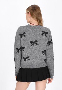 Maglione grigio a maglia con motivi a fiocco in paillettes nere, scollo rotondo e maniche lunghe, abbinato a una gonna plissettata nera.