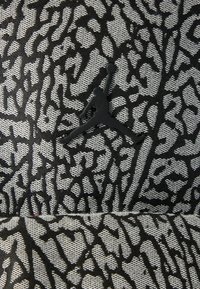 Μαύρο και γκρι καπέλο με υφασμένο σχέδιο και έντονες, αφηρημένες γραμμές. Περιλαμβάνει μαύρο λογότυπο Jumpman σε αθλητική στάση.