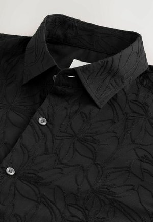 Camisa negra con un patrón floral bordado, con cuello puntiagudo y cierre de botones. La tela tiene un acabado texturizado y mate.