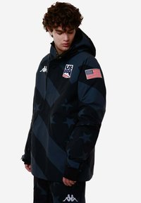 Giacca nera con cappuccio caratterizzata da un motivo a stelle, un'applicazione della bandiera degli Stati Uniti e un logo. Realizzata in materiale resistente alle intemperie con una vestibilità comoda.