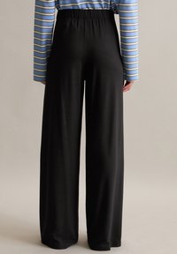 Pantalons noirs à jambes larges avec une ceinture élastique et une texture lisse, associés à un haut à manches longues rayé bleu et gris.