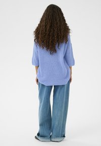 Pull bleu clair oversize à manches trois-quarts, tricot texturé, associé à un jean en denim clair à jambes larges avec ourlets retroussés.