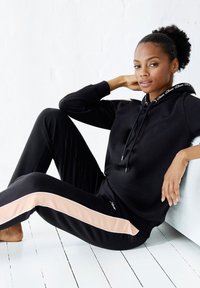 Schwarzes Sportoutfit mit einem Kapuzenpullover und Jogginghosen. Die Jogginghosen haben einen hellrosa Streifen an den Seiten und eine weiche Stofftextur.