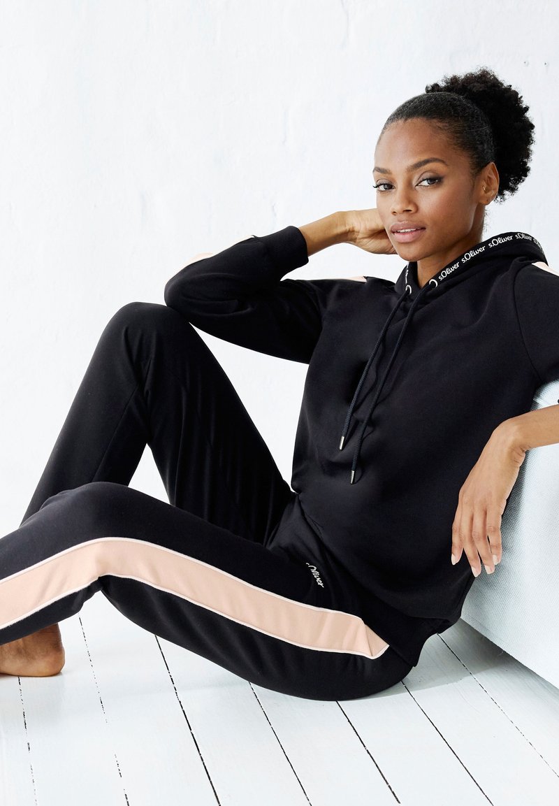 Schwarzes Sportoutfit mit einem Kapuzenpullover und Jogginghosen. Die Jogginghosen haben einen hellrosa Streifen an den Seiten und eine weiche Stofftextur.