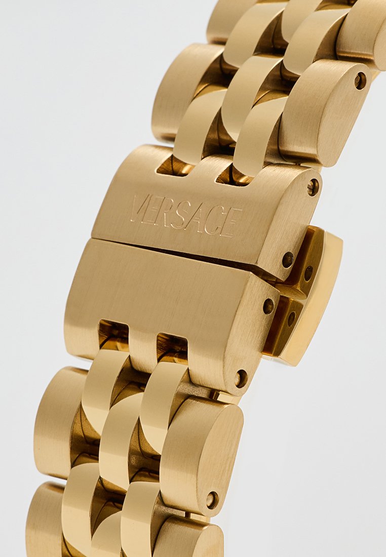 Pulsera de metal dorado con eslabones entrelazados. Presenta un acabado pulido y el logo grabado "VERSACE" en el cierre. Bordes redondeados, ancho medio.