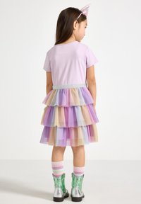 Lila t-shirt med en flerskiktad tyllkjol i pastellfärger, silverfärgat midjeband och gröna metalliska ankelstövlar med randiga strumpor.