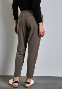 Pantalon vert olive, coupe slim, avec poches arrière et texture lisse. Associé à des baskets blanc cassé avec des accents noirs.