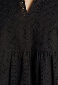 Tissu noir avec motif œillet brodé, avec un col en V et une couture froncée sous la poitrine.