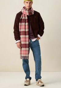 Bruine corduroy jas, paarse trui, blauwe jeans en een roze geruite sjaal met franjes. Beige sneakers met bruine en rode accenten.