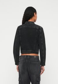 Μαύρο τζιν κοντό μπουφάν με γιακά, μακριά μανίκια και διακριτική φθορά. Συνδυάζεται με αντίστοιχο μαύρο παντελόνι cargo με τσέπες.