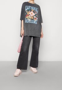 Camiseta gráfica gris de gran tamaño con un vibrante diseño floral y texto, combinada con jeans de pierna ancha negros y zapatillas rosas. Accesorio de bolso rosa.