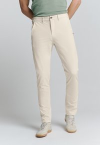 Beige chino broeken met een slim fit, voorzien van voorzakken, een knopen sluiting en een gladde textuur. Gecombineerd met lichtgekleurde sneakers.