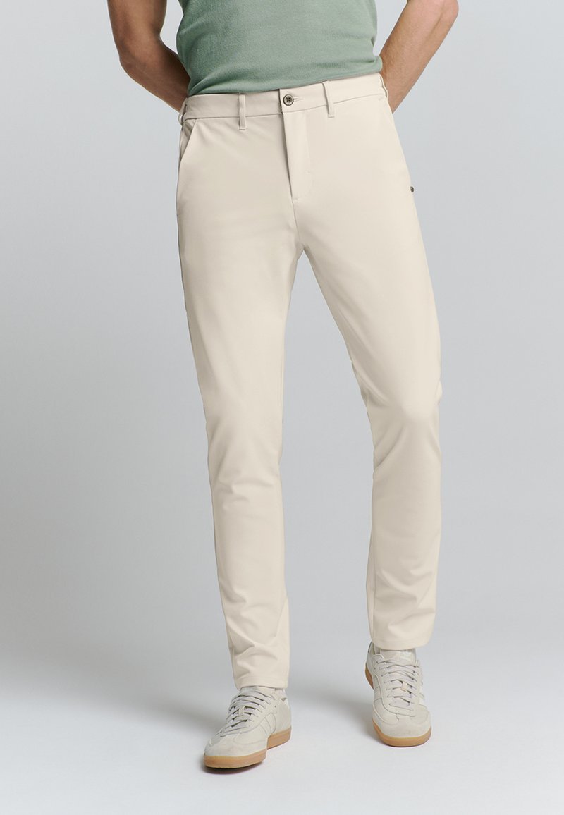 Beige chino broeken met een slim fit, voorzien van voorzakken, een knopen sluiting en een gladde textuur. Gecombineerd met lichtgekleurde sneakers.