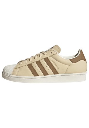 Beige leather sneaker with brown stripes, rubber toe cap, and textured heel detail. Features a white sole and lace-up design.