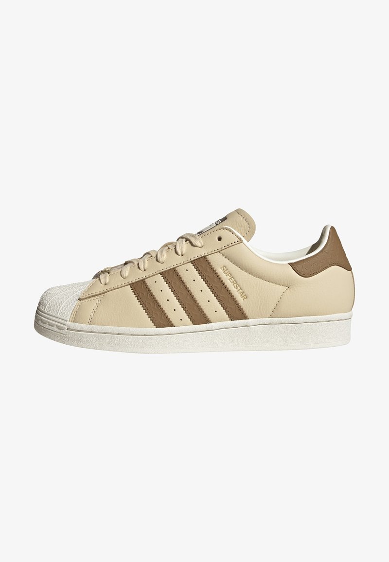 Beige leather sneaker with brown stripes, rubber toe cap, and textured heel detail. Features a white sole and lace-up design.