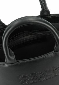 Zwarte leren handtas met dubbele handvatten aan de bovenkant, ritssluiting aan de binnenkant en een reliëflogo op de buitenkant. Glad oppervlak met een ronde vorm.