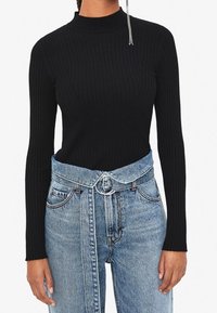 Top nero a maniche lunghe con fantasia a coste e collo alto, abbinato a jeans azzurri a vita alta con dettaglio di cintura circolare.