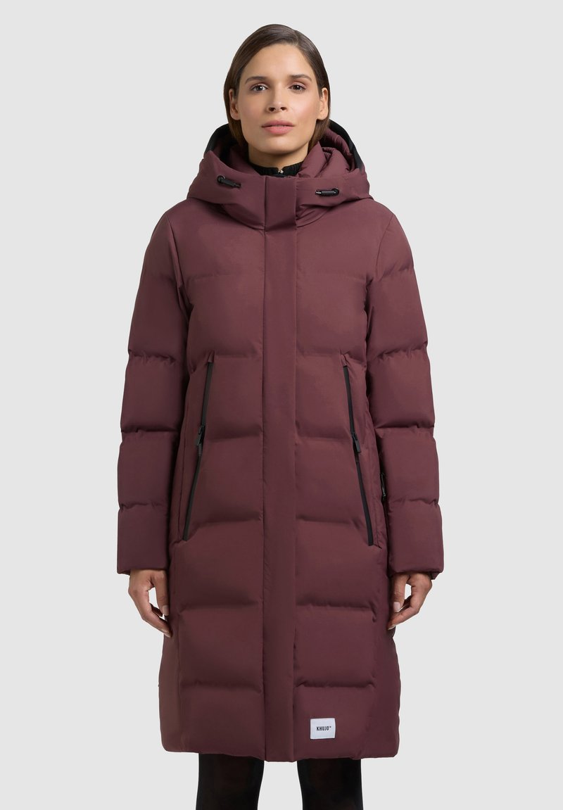 Tumepunane kapuutsiga sulejope, millel on kõrge kaelus, lukuga taskud ja isoleerimiseks tikkimismuster.