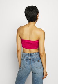 Top fucsia tagliato senza spalline con texture arricciata abbinato a jeans in denim azzurri a vita alta, con design classico a cinque tasche.