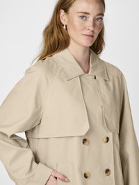 Beige trench coat laget av lett stoff med dobbel knepping, stor krage og hornknapper, med sidelommer.