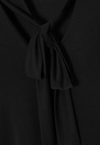 Čierna tkanina s jemnou textúrou, zdobená uzlovým detailom na výstrihu a hlbokým výstrihom do V. Jednoduché a minimalistické.