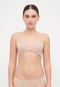 Beige padded bra with adjustable thin straps and a smooth texture. Features a central seam and a seamless design for a discreet fit.
