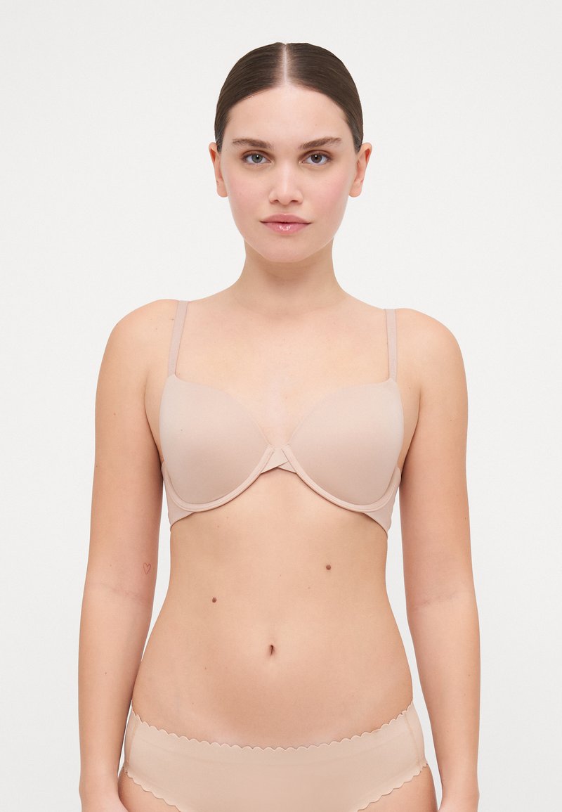 Beige padded bra with adjustable thin straps and a smooth texture. Features a central seam and a seamless design for a discreet fit.