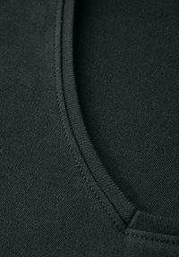 Tissu en coton vert foncé avec une texture lisse, présentant une encolure arrondie et des coutures soignées le long des bords.