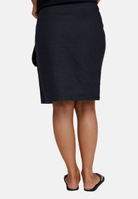 Mørk marineblå linje blyantskjørt med rett snitt, kne-lengde kant og subtil tekstur. Brukt med svarte flip-flops.