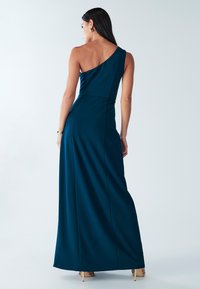 Vestido largo de un solo hombro en verde azulado profundo, hecho de tela suave. Cuenta con un corsé ajustado y una falda fluida con una sutil abertura trasera.