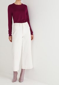 Krusbärsfärgad långärmad topp med rund halsringning, matchad med vida vita byxor och ljuslila högklackade stövlar.