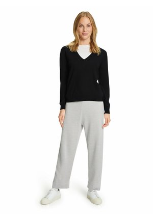 Schwarzer V-Ausschnitt-Pullover mit engeren Bündchen, kombiniert mit hellgrauten weit geschnittenen Hosen und weißen Sneakern. Glatte Textur, lässiges Design.