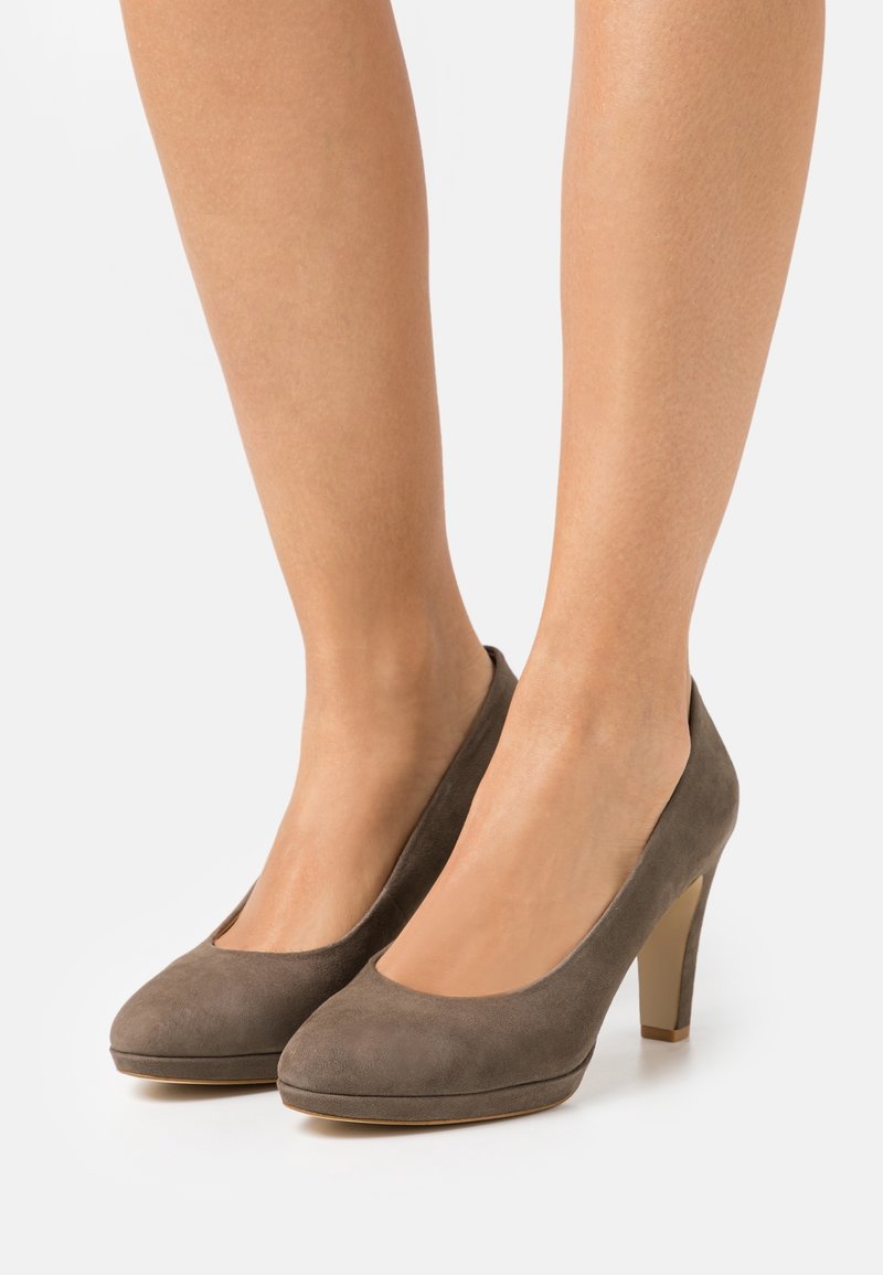 Escarpins en daim marron à bout rond portés pieds nus sur fond blanc.