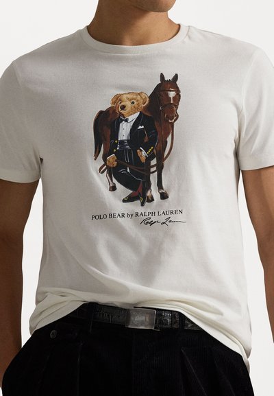 Valge lühikeste varrukatega t-särk, millel on illustratsioon frakis karust koos hobusega, detailne joonistus värvide ja peente joontega. Eesmine graafiline kujundus.