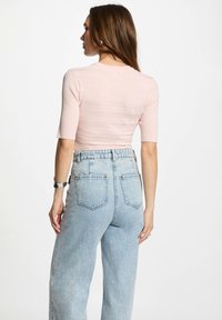 Top corto ribbed rosa chiaro con scollatura rotonda e maniche corte, abbinato a jeans in denim chiaro a vita alta con tasche posteriori.