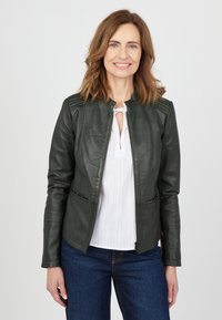 Grön läderjacka med en figurnära design, ribbade axelaccenter och dragkedjestängning. Kombinerad med en vit blus och blå jeans.