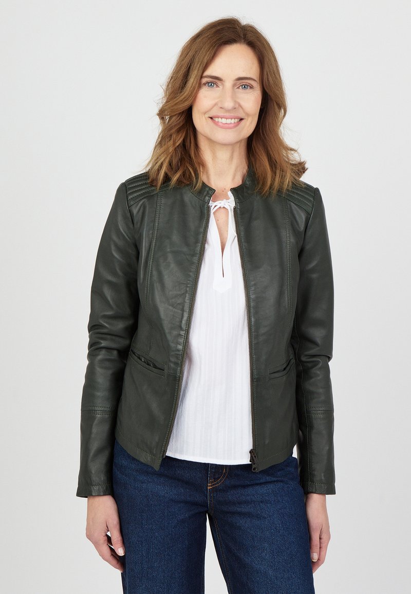 Grön läderjacka med en figurnära design, ribbade axelaccenter och dragkedjestängning. Kombinerad med en vit blus och blå jeans.