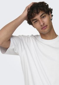 Witte katoenen t-shirt met een ronde halslijn en korte mouwen, met een relaxte pasvorm en zachte textuur, gedragen door een jonge man.