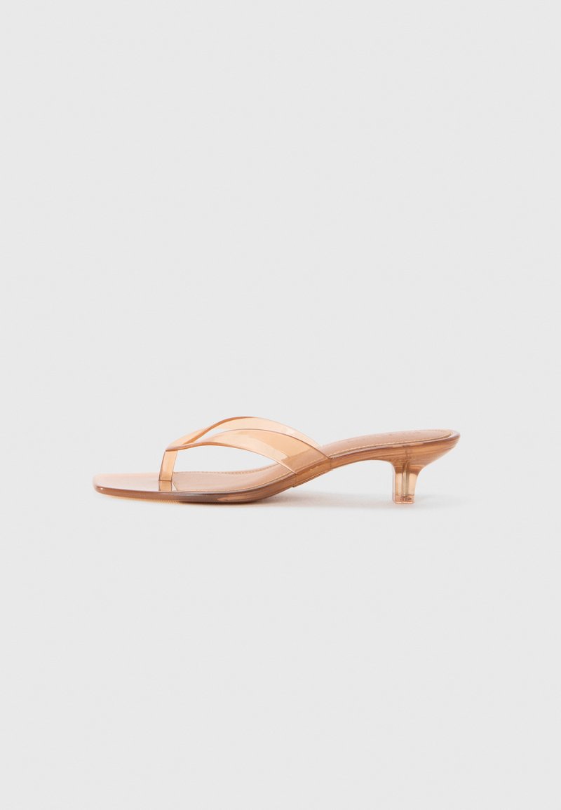 Sandale nu-pourpre transparente avec un petit talon de chat et de fines lanières transparentes sur un fond blanc.