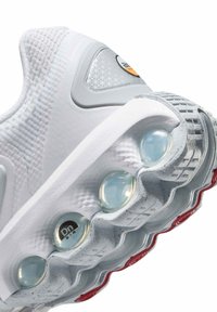 Zapatilla deportiva blanca con parte superior de malla texturizada, acentos grises, cápsulas de amortiguación transparentes y una suela de goma con patrón que presenta detalles rojos.