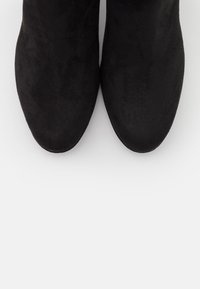 Stivaletti neri in suede con punta affusolata, texture liscia e senza hardware o motivi visibili. La vista dall'alto mostra un design semplice.