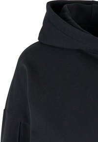 Sweat à capuche noir avec une grande capuche et un détail en tissu côtelé sur l'épaule et la partie supérieure du bras.