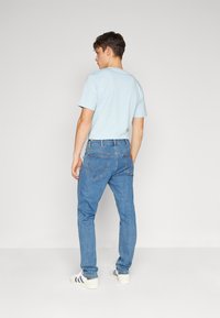 Camiseta de color azul claro, diseño ajustado. Vaqueros de mezclilla azul con costuras visibles y detalles en los bolsillos. Zapatillas deportivas blancas casuales con rayas negras.